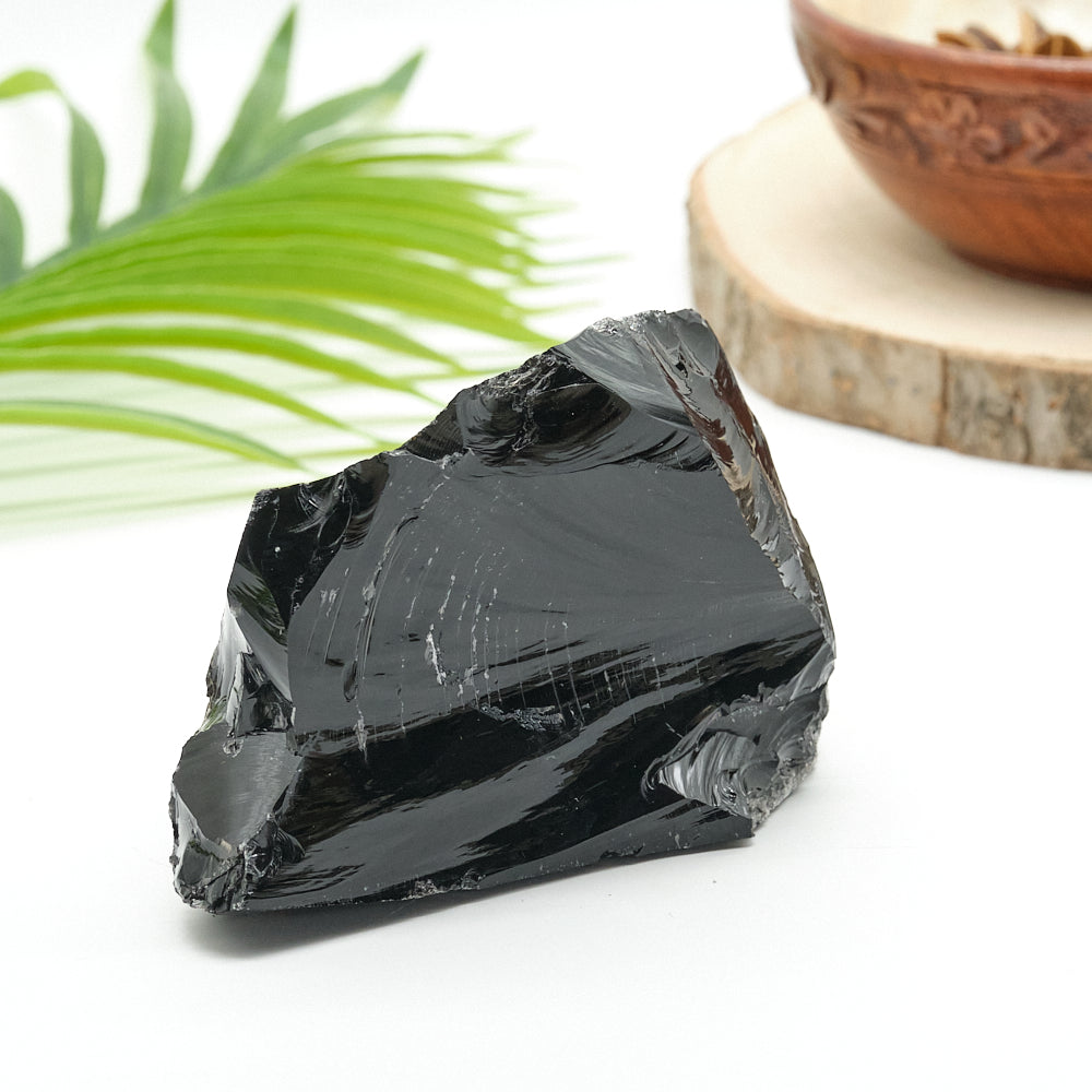 Black obsidian stone on a white surface with a wooden bowl and green leaf in the background