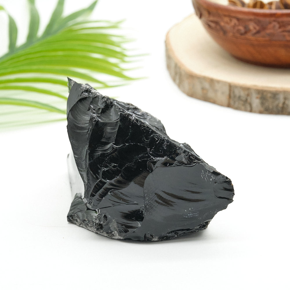 Black obsidian stone on a white surface with a wooden bowl and green leaf in the background