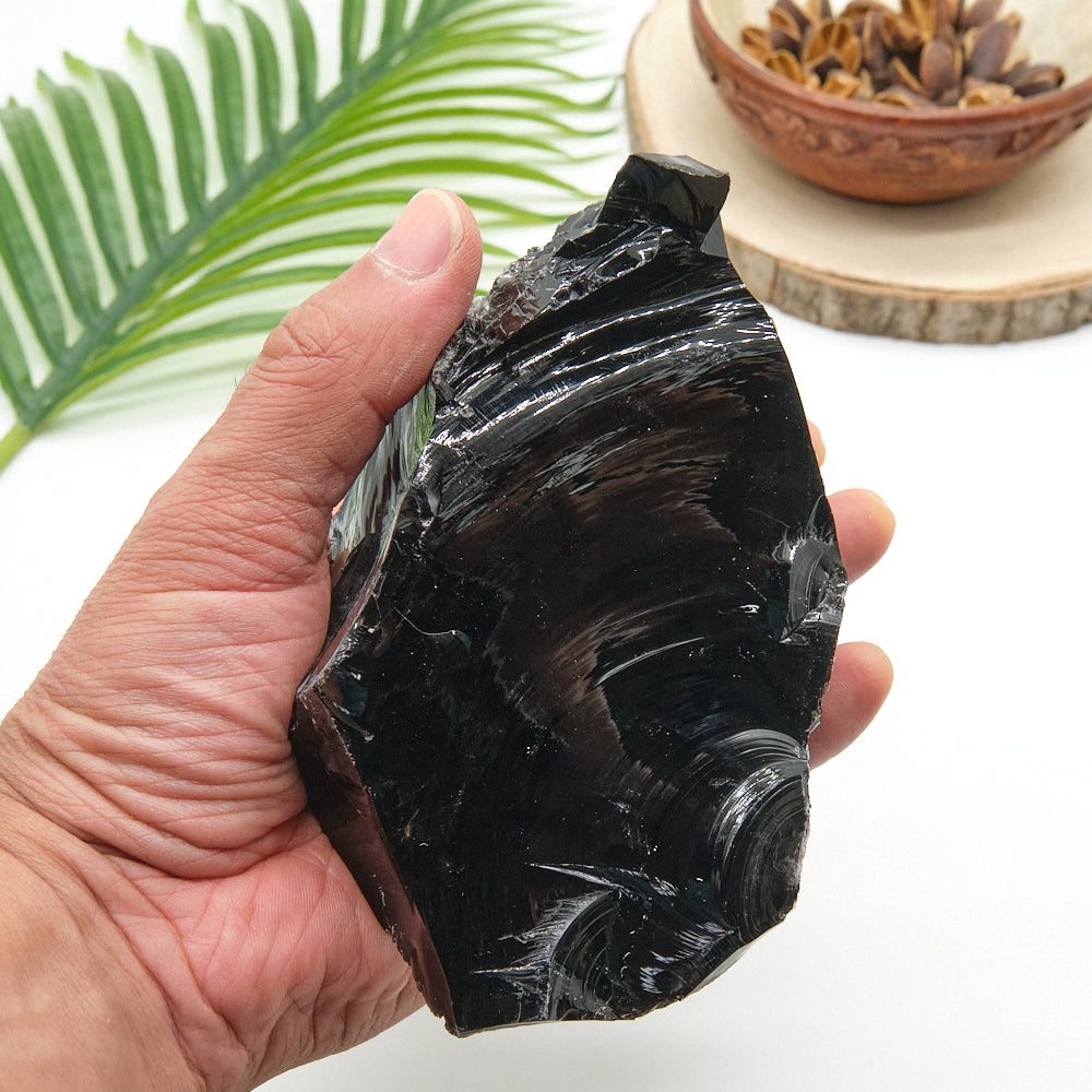 Hand holding a large black obsidian crystal with a leaf and bowl in the background