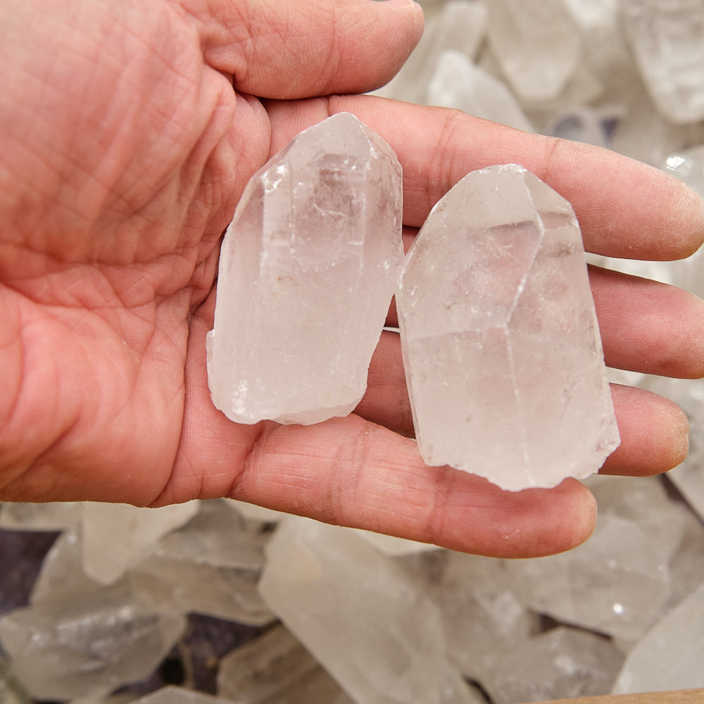 Hand holding two clear crystal points with a blurred background of more crystals.