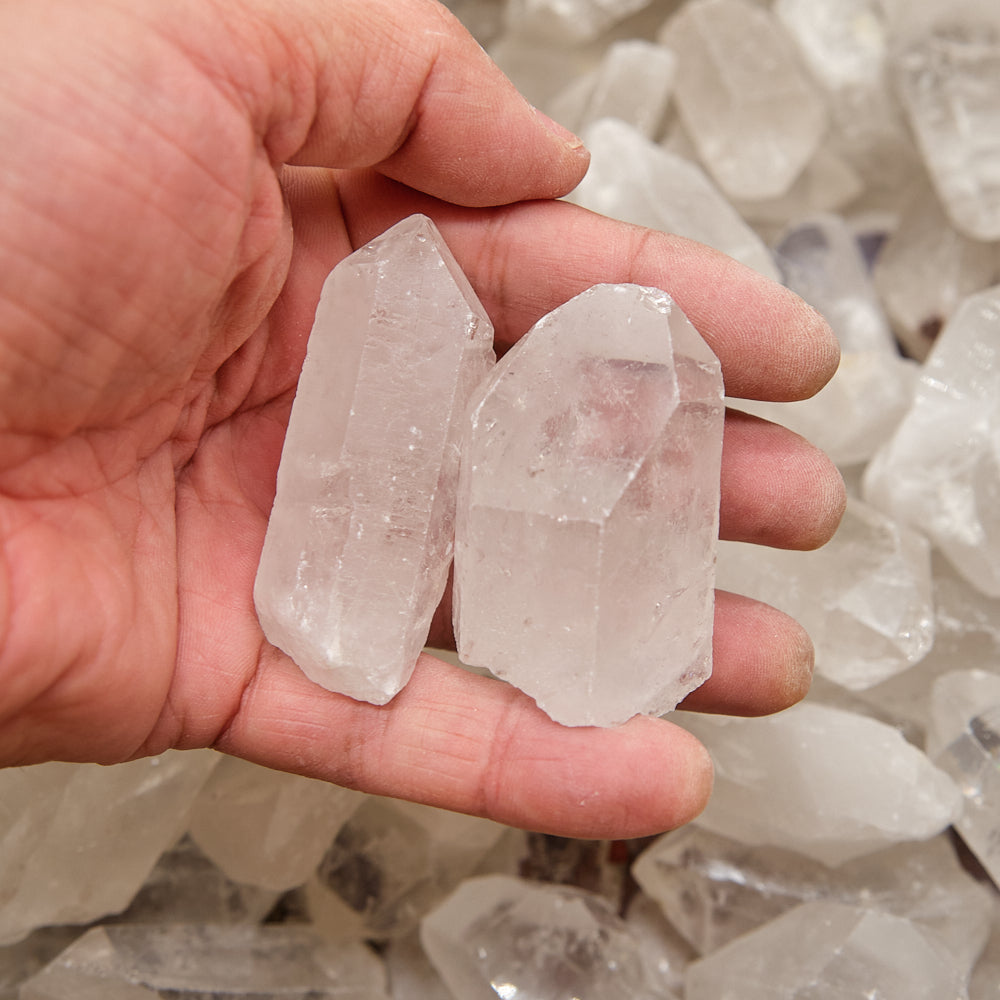 Hand holding two clear crystal points with a background of more crystals.