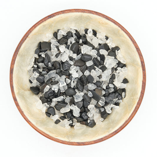 Small bowl filled with black, white, crystals, tourmaline and clear quartz on a white background