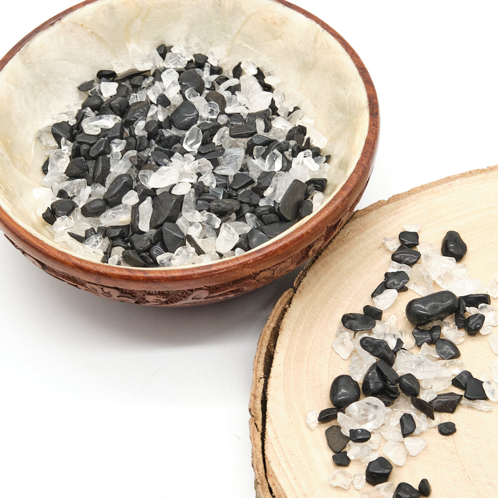 Small bowl filled with black, white, crystals, tourmaline and clear quartz on a white background