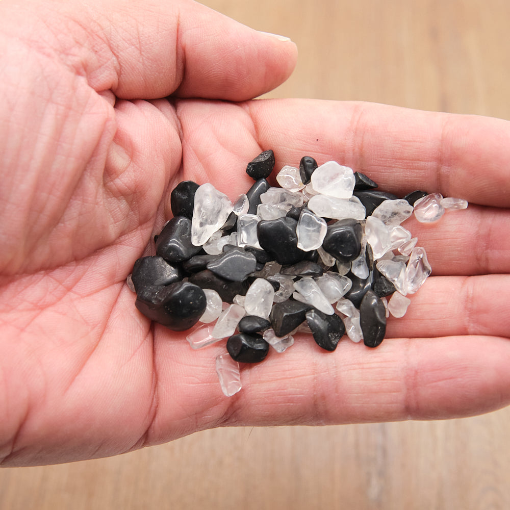 Hand holding a small pile of black and clear stones on a wooden surface