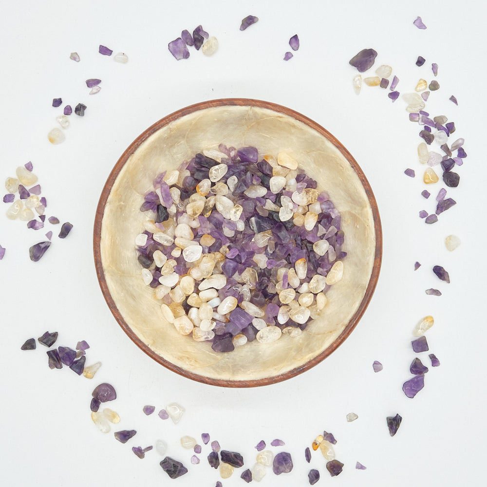 Small bowl filled with amethyst and citrine stones on a light surface with scattered stones
