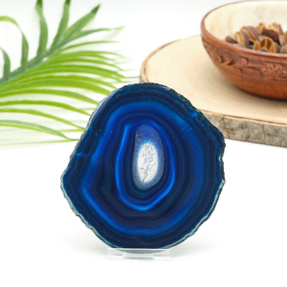Blue agate stone on a white surface with a plant and wooden bowl in the background