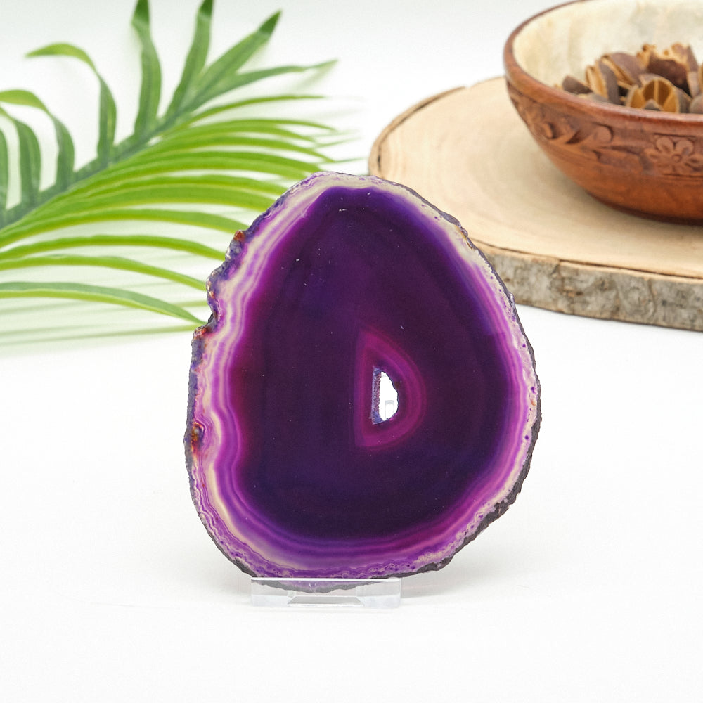 Purple agate stone on a white background with a plant and wooden bowl in the background