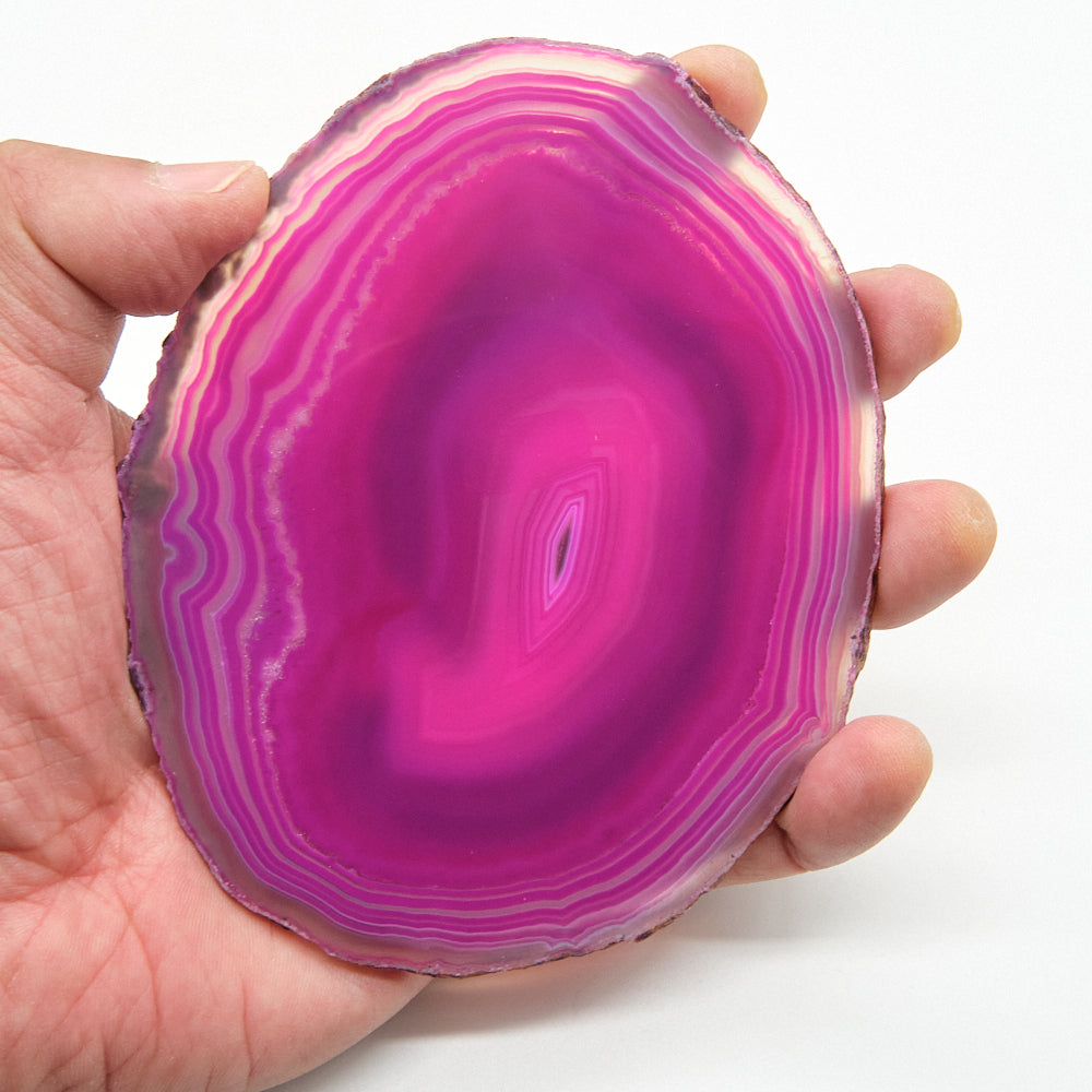 Hand holding a vibrant pink and purple agate slice against a white background