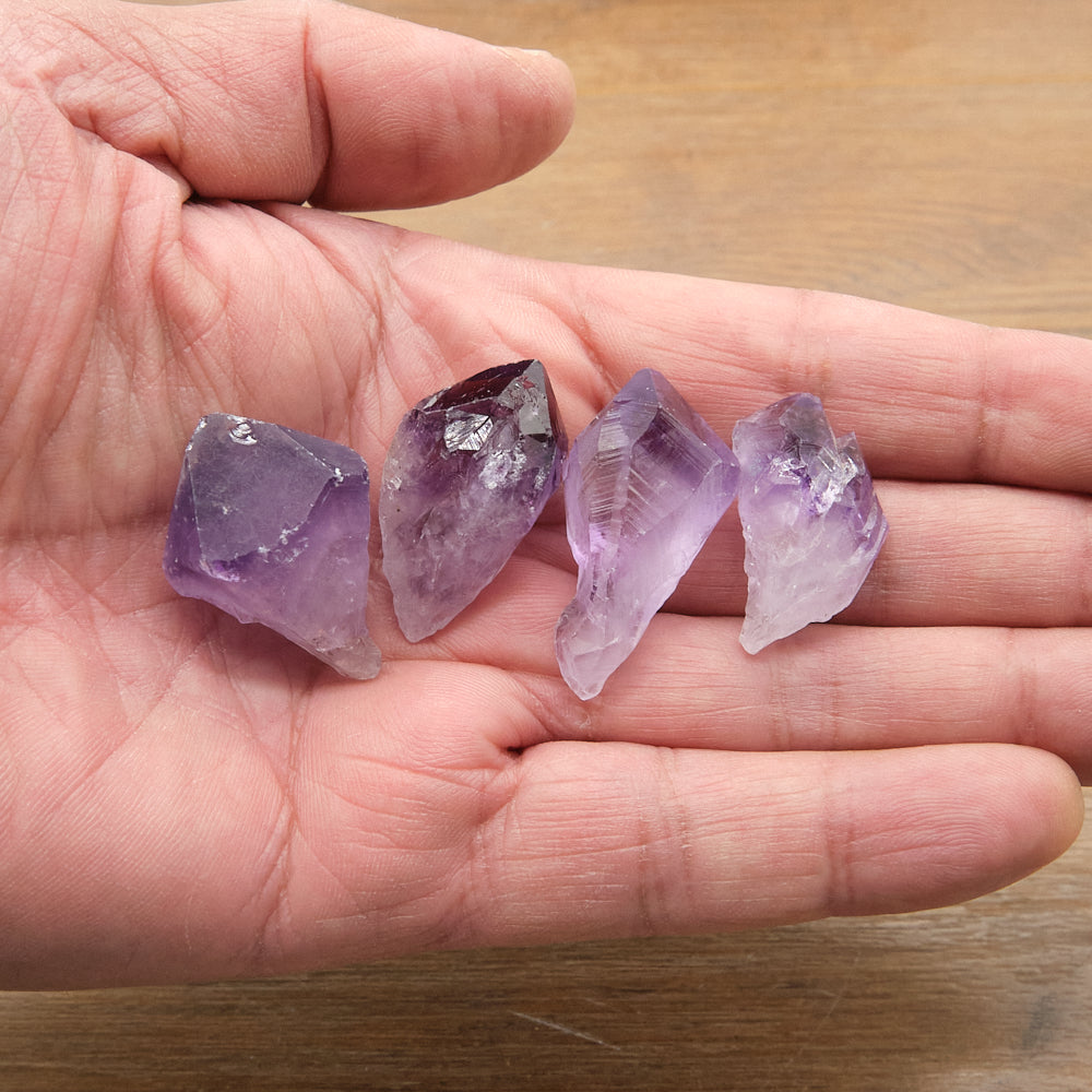 Four amethyst crystals held in a hand on a wooden surface