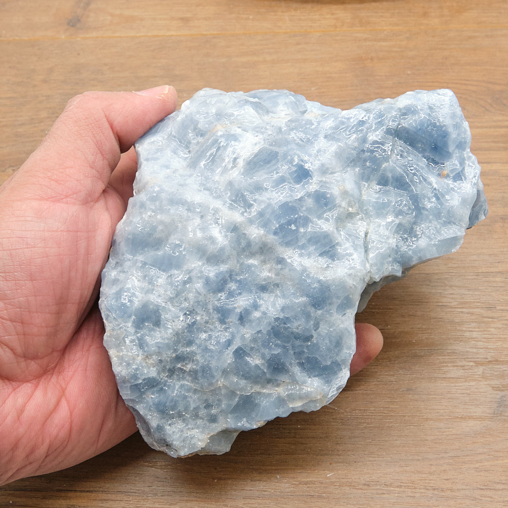 Hand holding a large blue calcite stone on a wooden surface