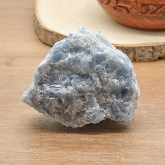Raw blue calcite stone on a wooden surface with a decorative bowl in the background