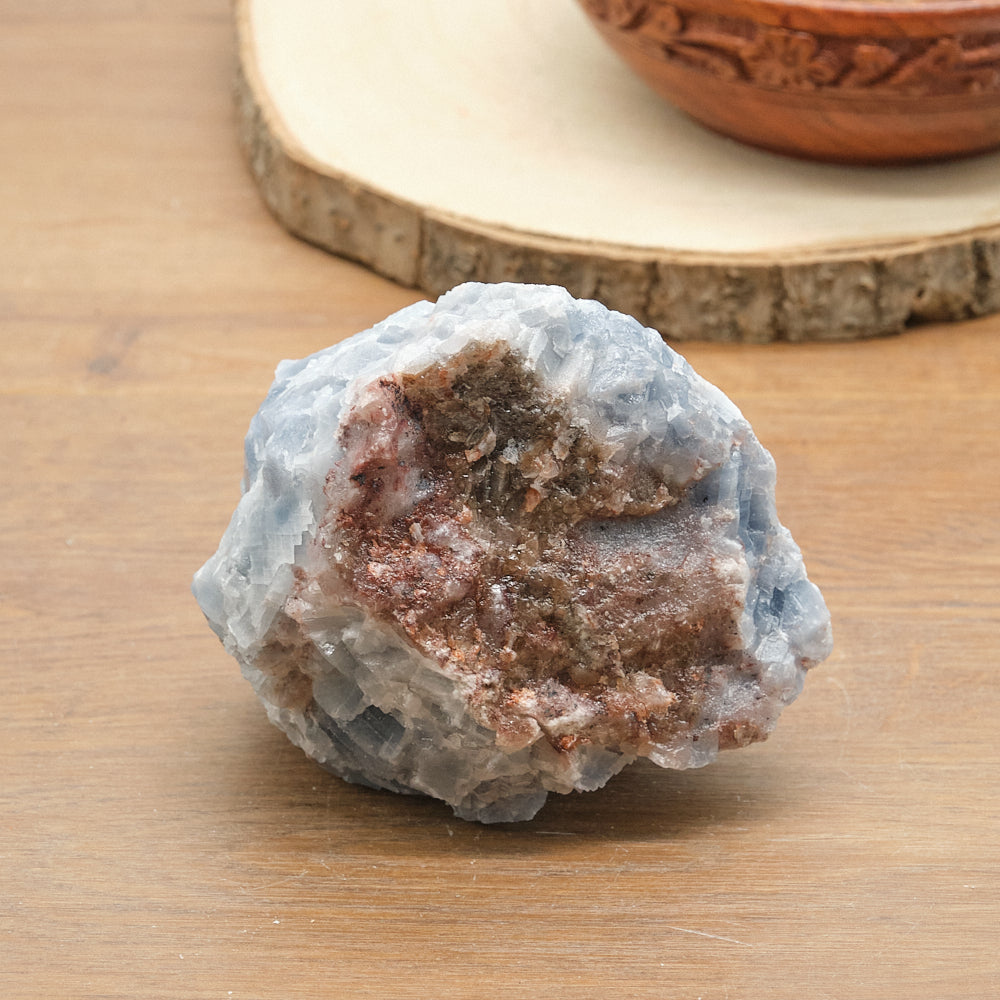 Raw calcite crystal rock on a wooden surface with a decorative bowl in the background