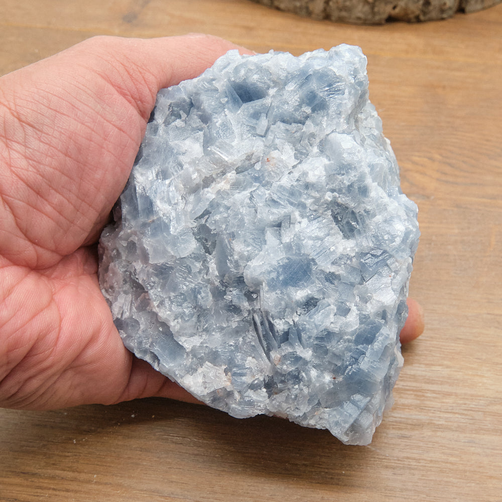 Hand holding a large blue calcite crystal on a wooden surface
