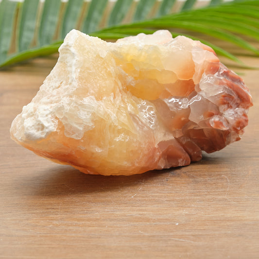 Raw yellow red calcite crystal rock on a wooden surface with green leaves in the background