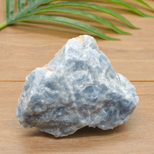 Raw blue calcite stone on a wooden surface with green leaves in the background