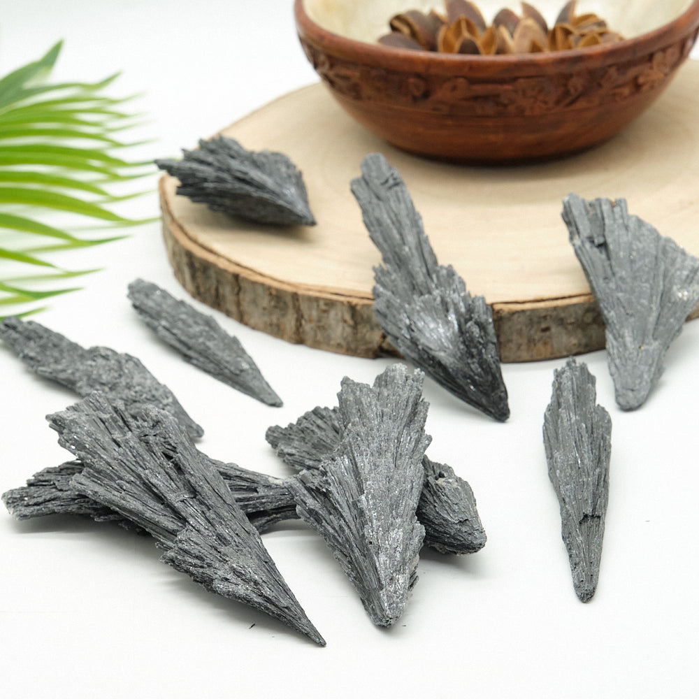 black kyanite fan crystals leaf-like structures on a white surface with a wooden bowl in the background.