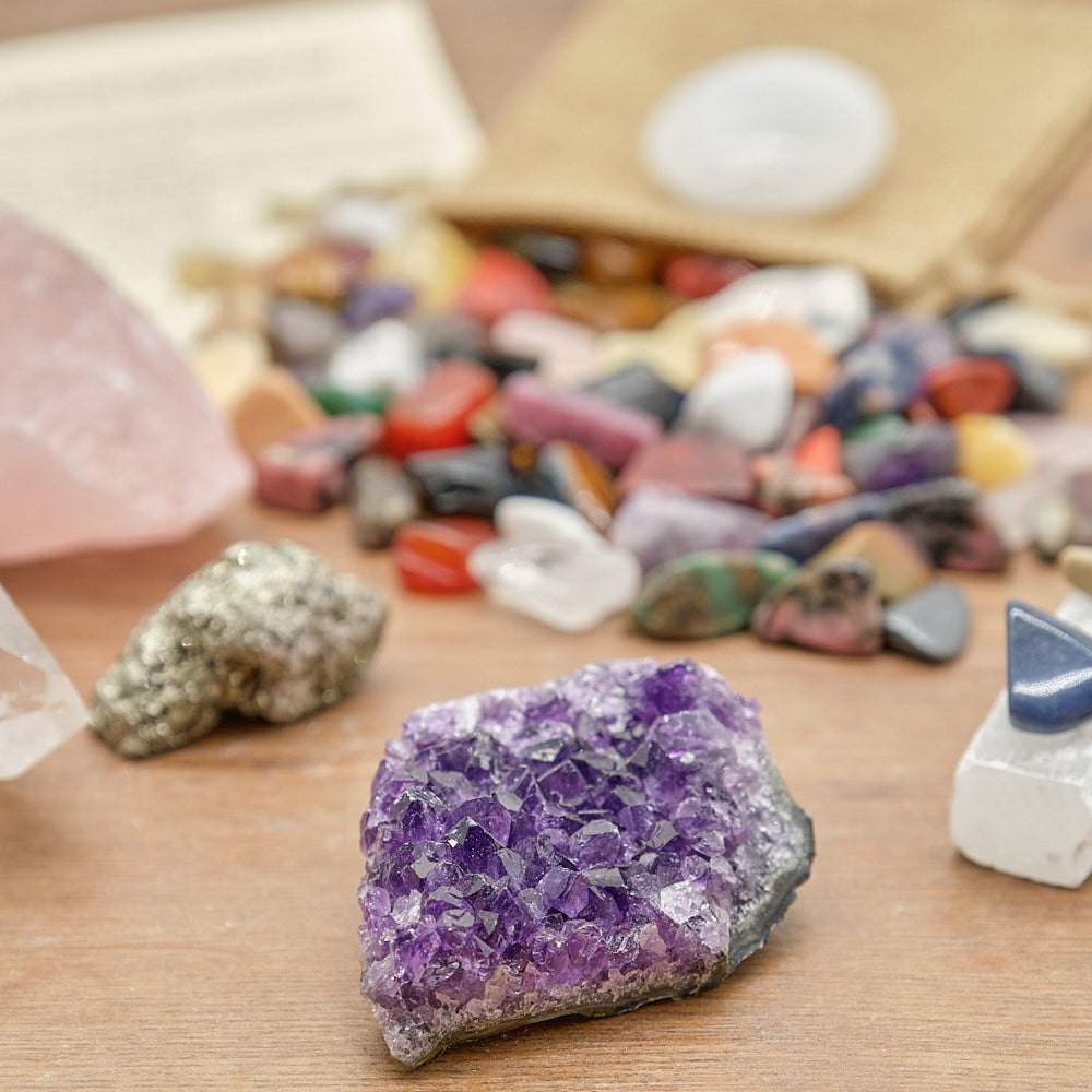 Close-up of a amethyst geode on a wooden surface with other crystals and a bag in the background.