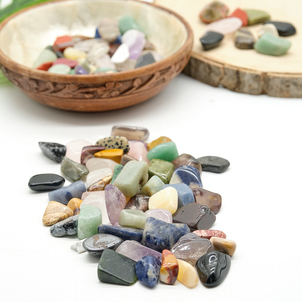 Assorted colorful crystal gemstones on a white surface with a wooden bowl in the background.