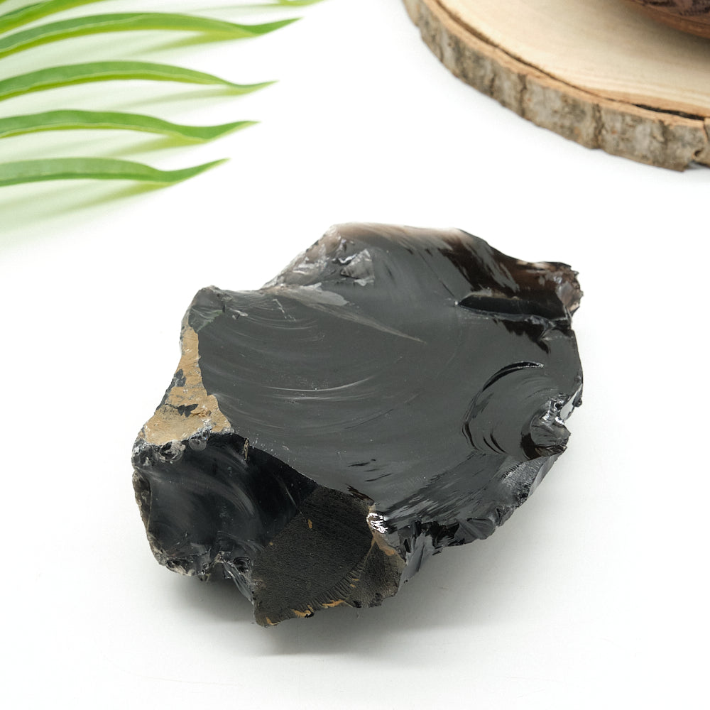 Black obsdian stone on a white surface with green leaves in the background