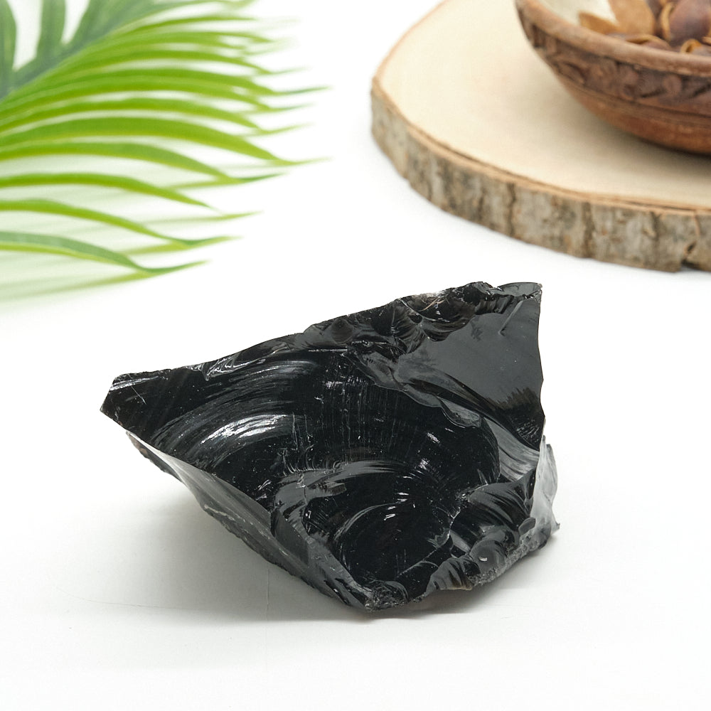 Black obsidian  stone on a white surface with a leaf and wooden object in the background