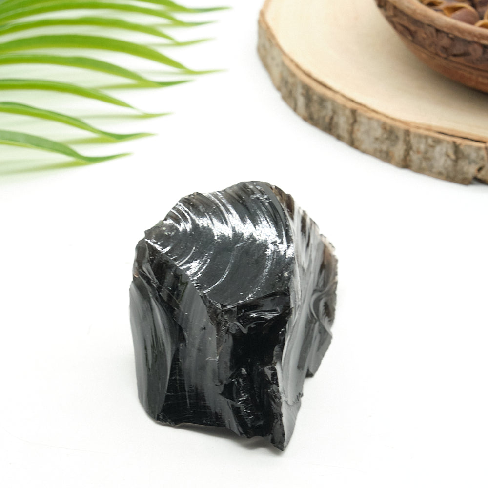 Black obsidian on a white background with green leaves and a wooden surface.