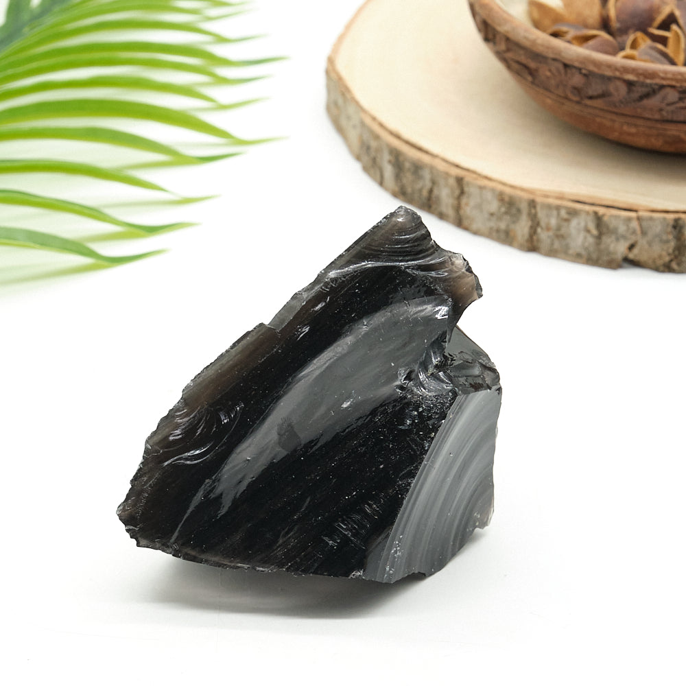 Black obsidian  stone on a white surface with a wooden board and green leaves in the background