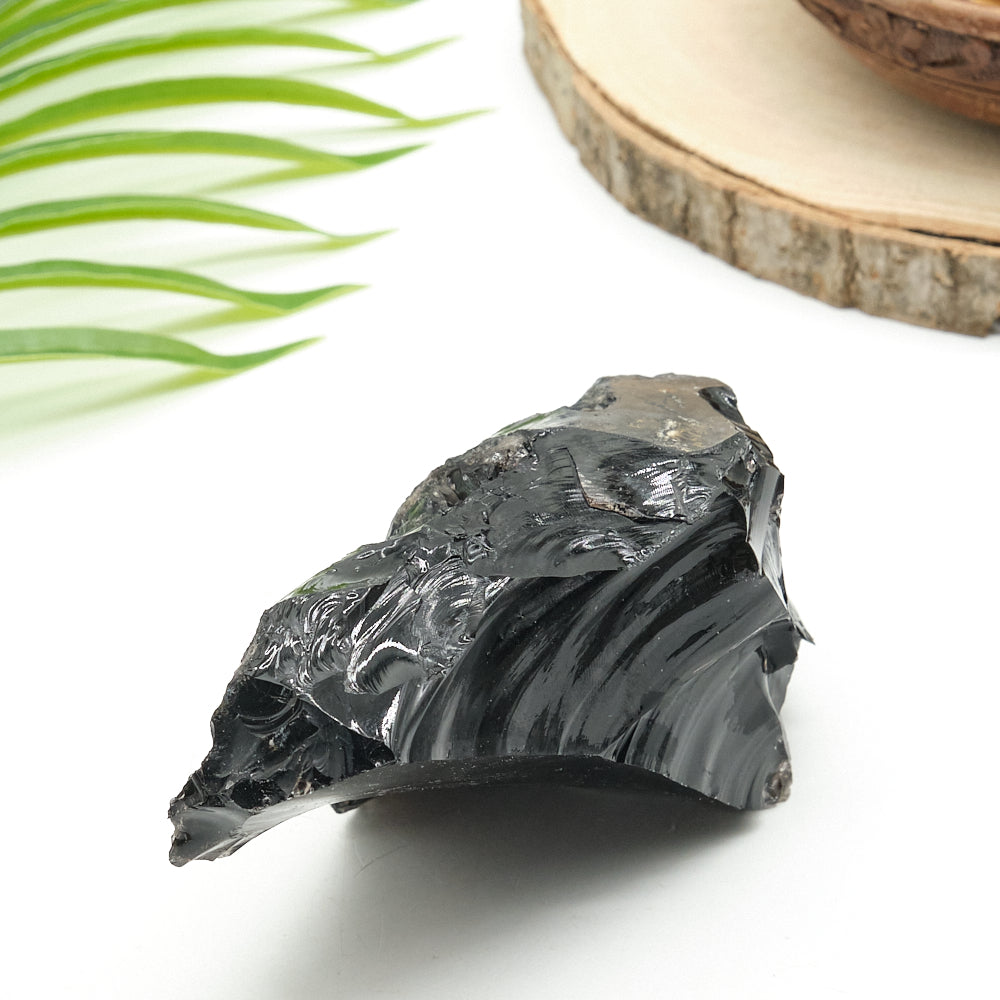 Black obsidian stone on a white surface with green leaves and a wooden slice in the background