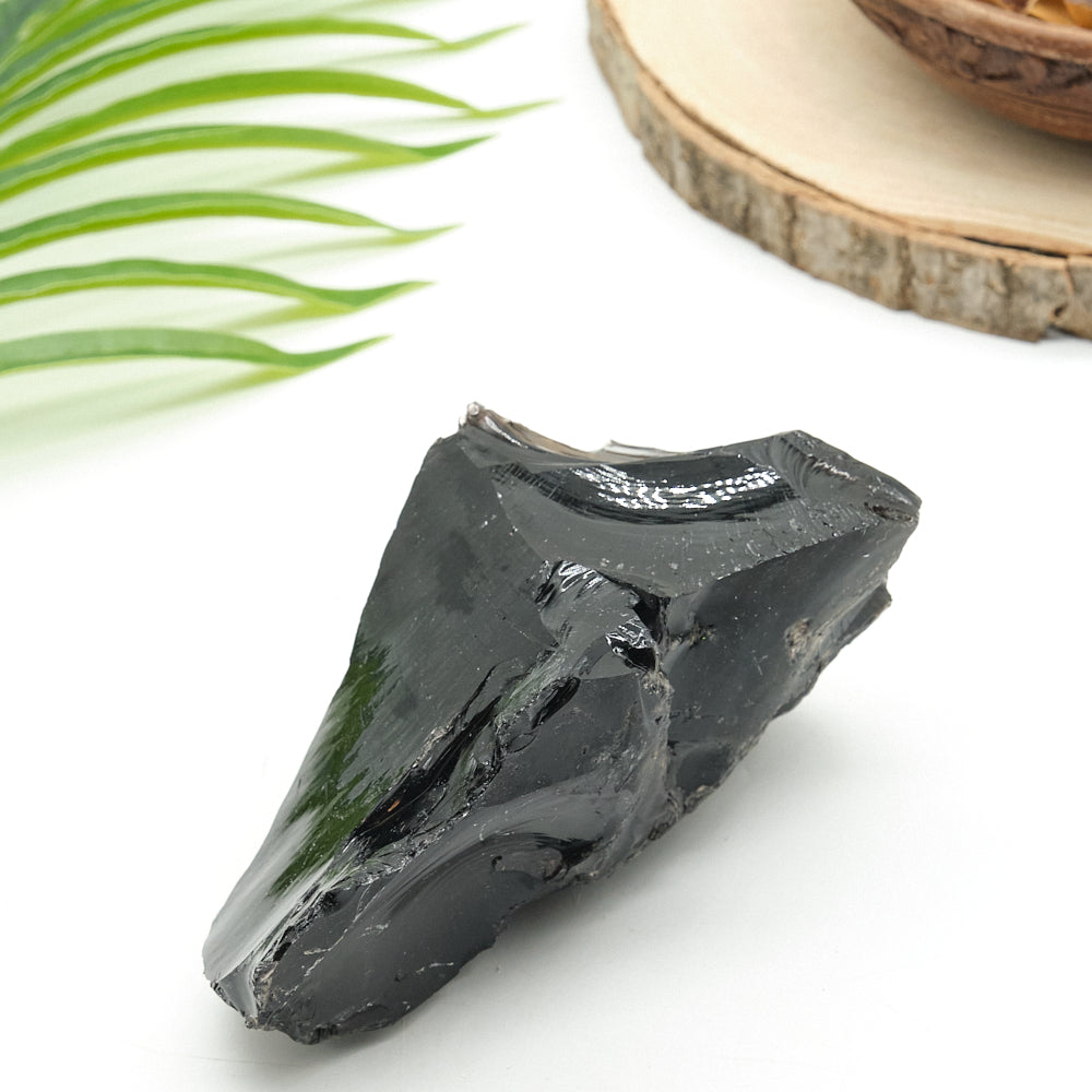 Black obsidian stone on a white surface with green leaves and a wooden slice in the background