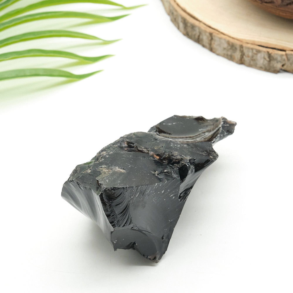 Black obsidian stone on a white surface with green leaves and a wooden slice in the background