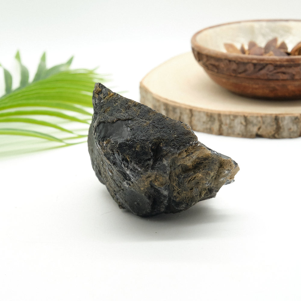 Large dark obsidian  stone on a white surface with a blurred background