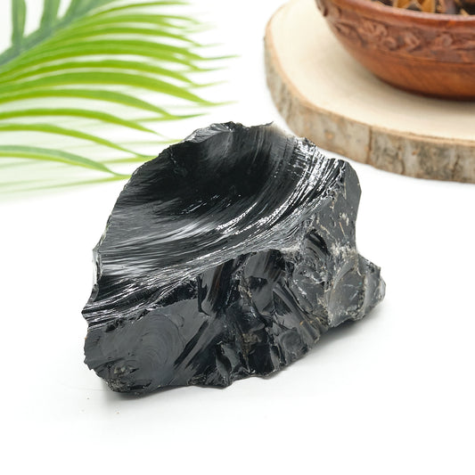 Black obsidian stone on a white surface with a wooden bowl and green leaf in the background
