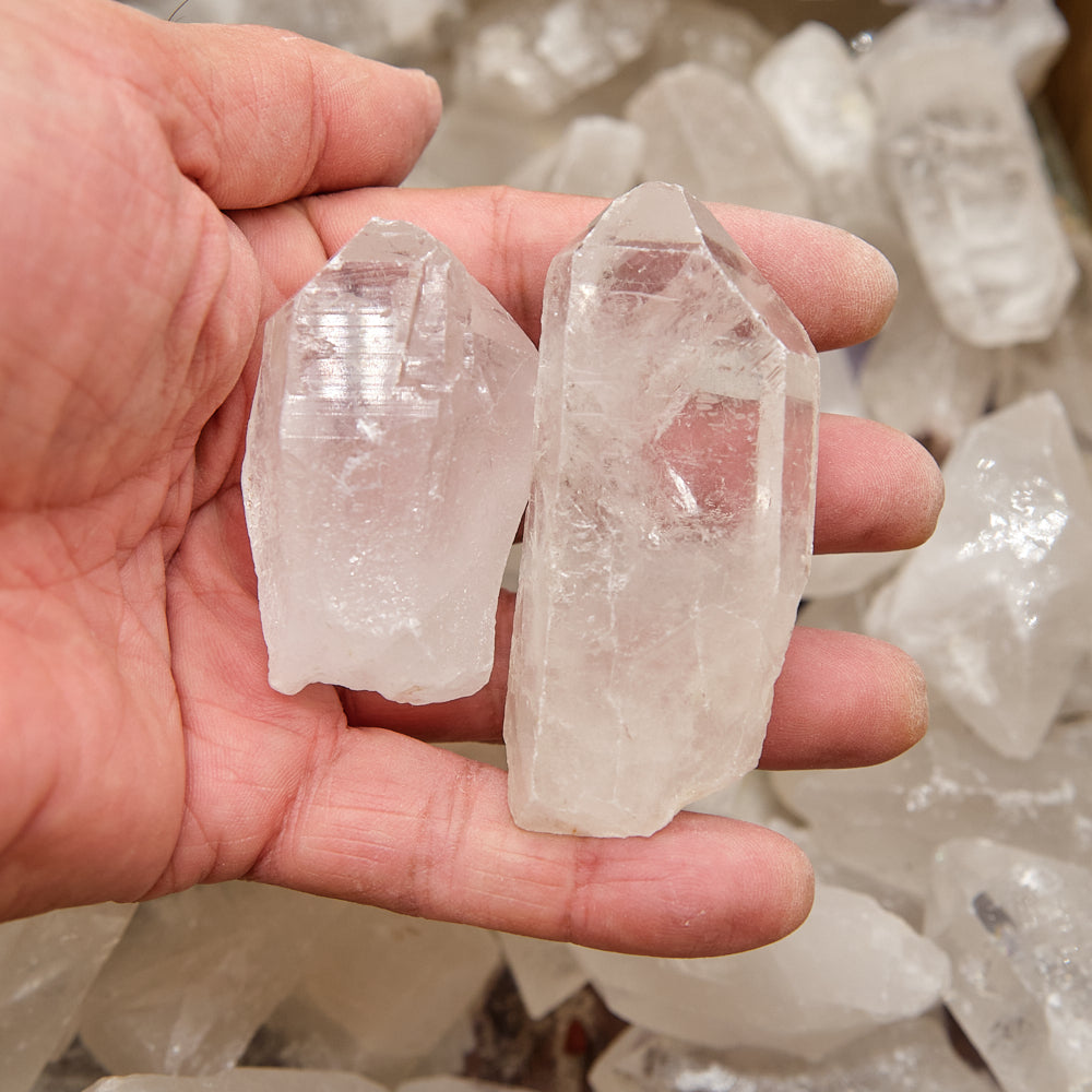 Hand holding two clear crystal points with a background of more crystals.