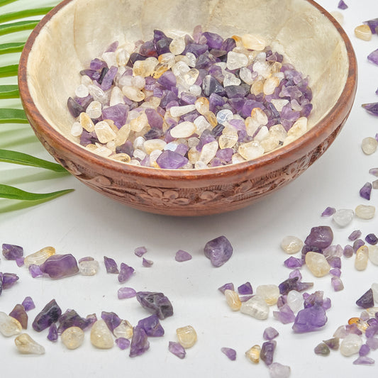Small bowl filled with amethyst and citrine stones on a light surface with scattered stones 