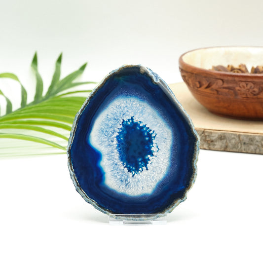 Blue and white agate crystal on a stand with a wooden bowl and green leaves in the background