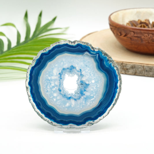 Blue and white agate crystal on a stand with a wooden bowl and green leaves in the background