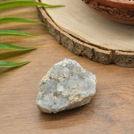 celestite Crystal rock on a wooden surface with leaves and a wooden bowl in the background