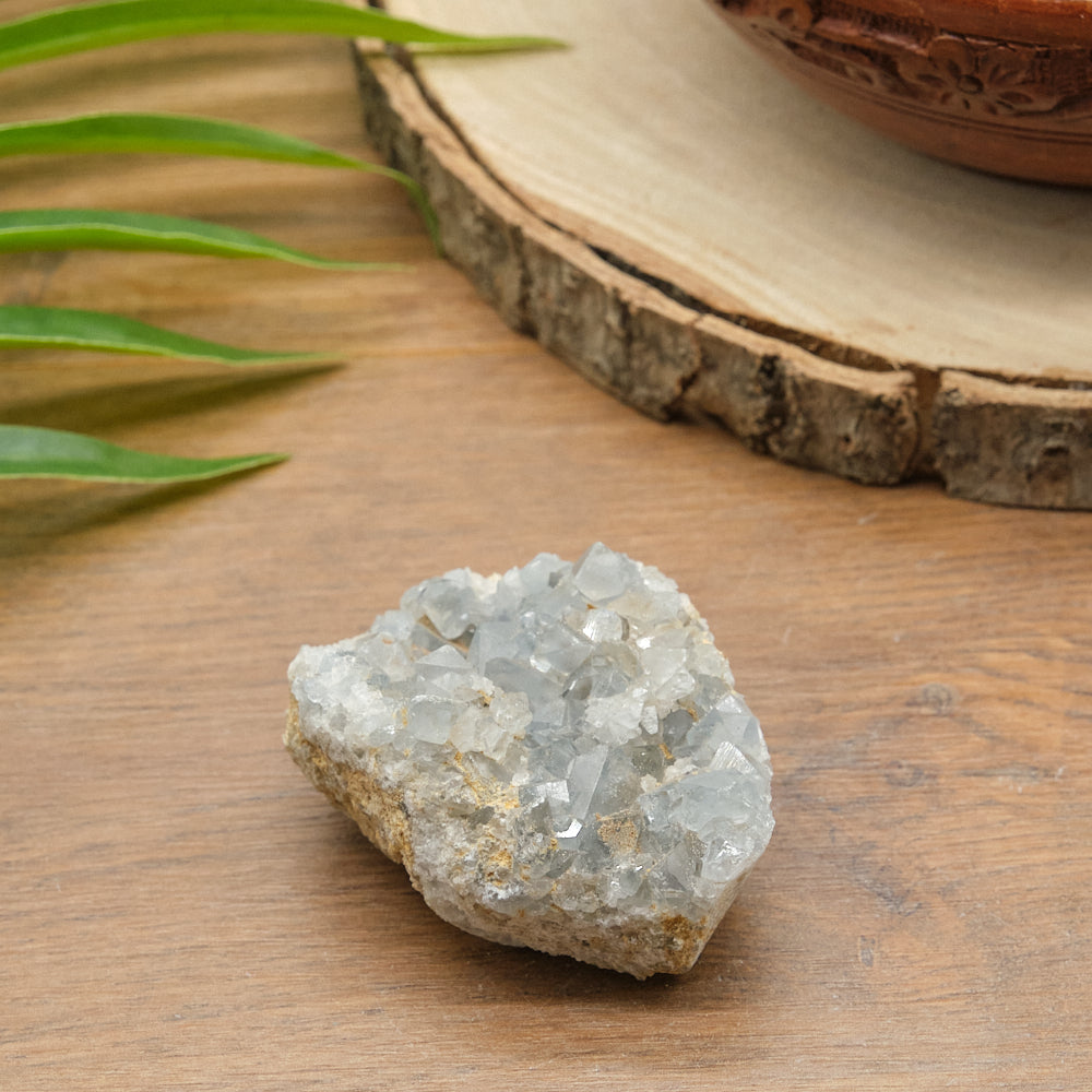 celestite Crystal rock on a wooden surface with leaves and a wooden bowl in the background
