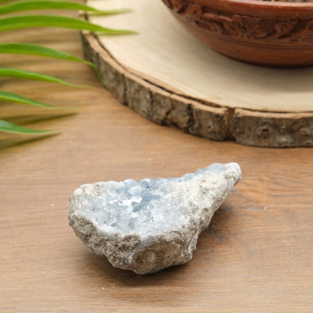 blue celestite Geode on a wooden surface with a terracotta pot in the background