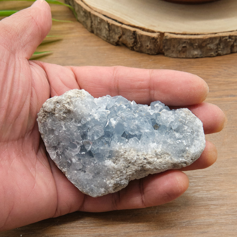 Hand holding a crystal celestite rock on a wooden surface
