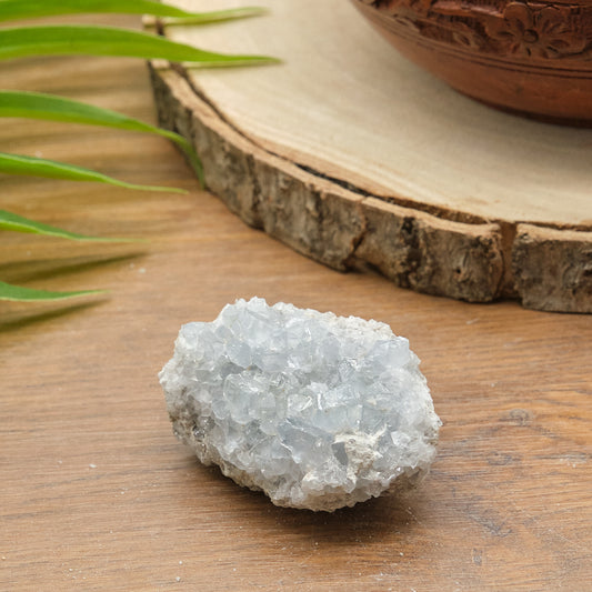 celestite Crystal cluster on a wooden surface with green leaves and a wooden bowl in the background