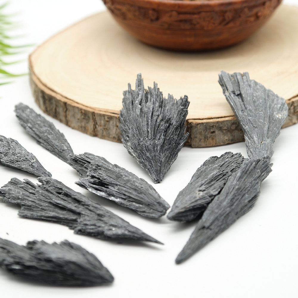  black kyanite fan crystals on a white surface with a wooden bowl in the background