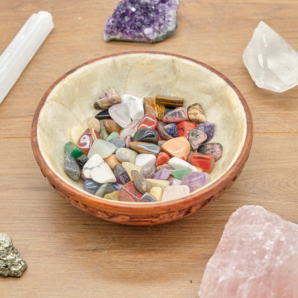 Decorative bowl filled with multicolored stones on a wooden surface with crystals around.