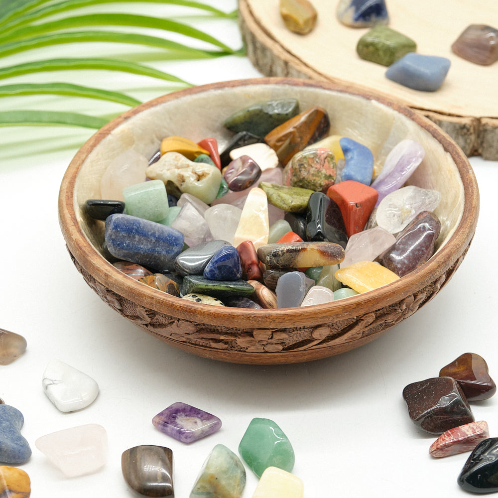 Wooden bowl filled with multicolored crystal gemstones on a white background