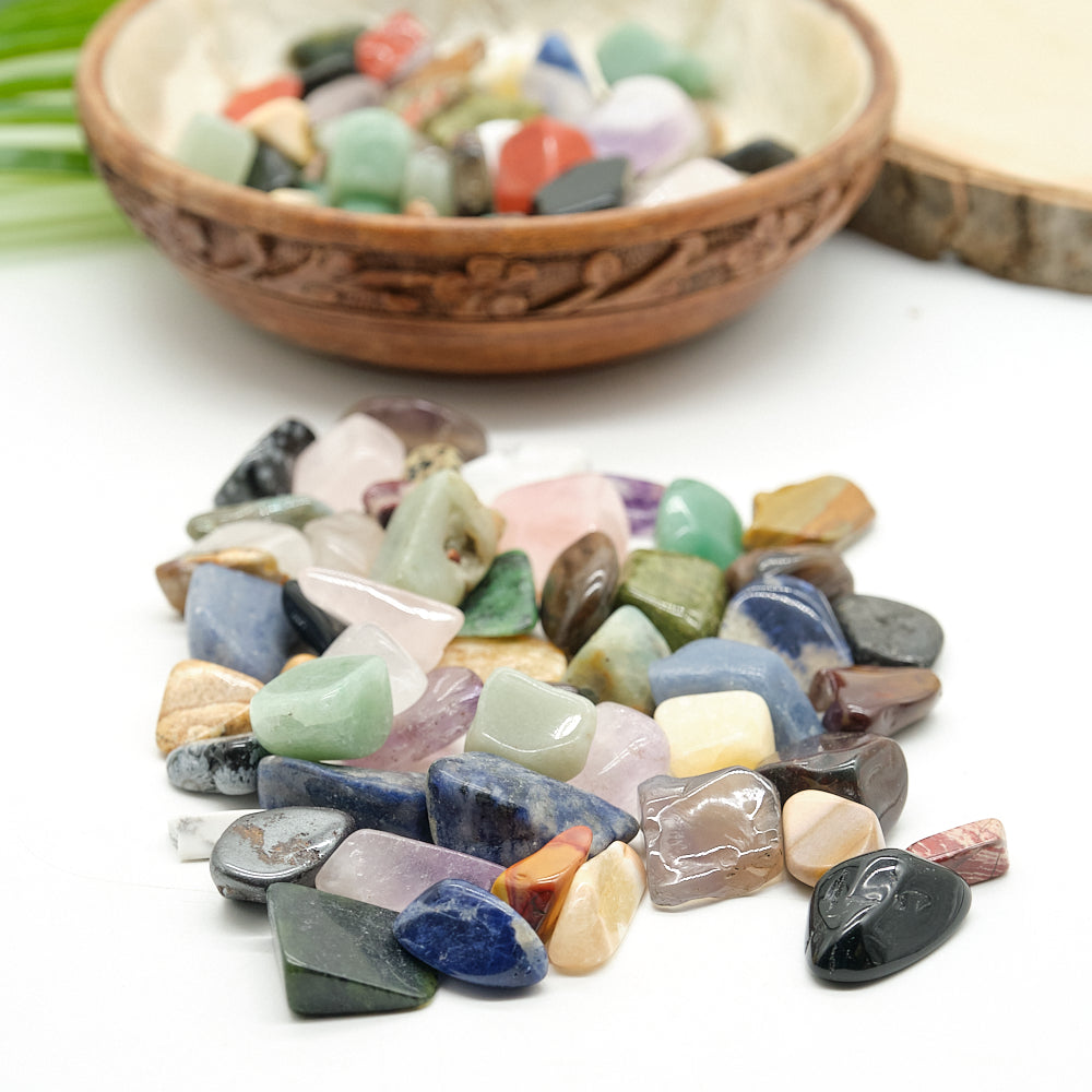 Assorted colorful crystal gemstones  on a white surface with a wooden bowl in the background.