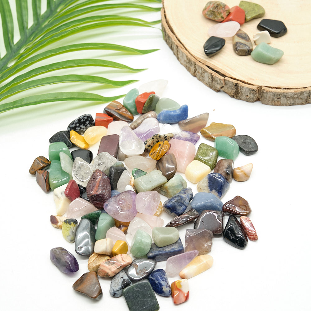 Assorted colorful crystal gemstones on a white surface with a wooden slice and green leaves in the background.