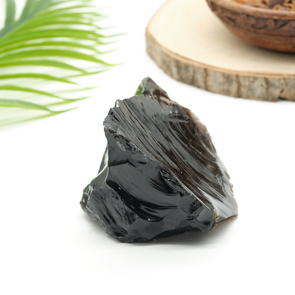 Black obsidian  crystal rock on a white surface with a blurred natural background