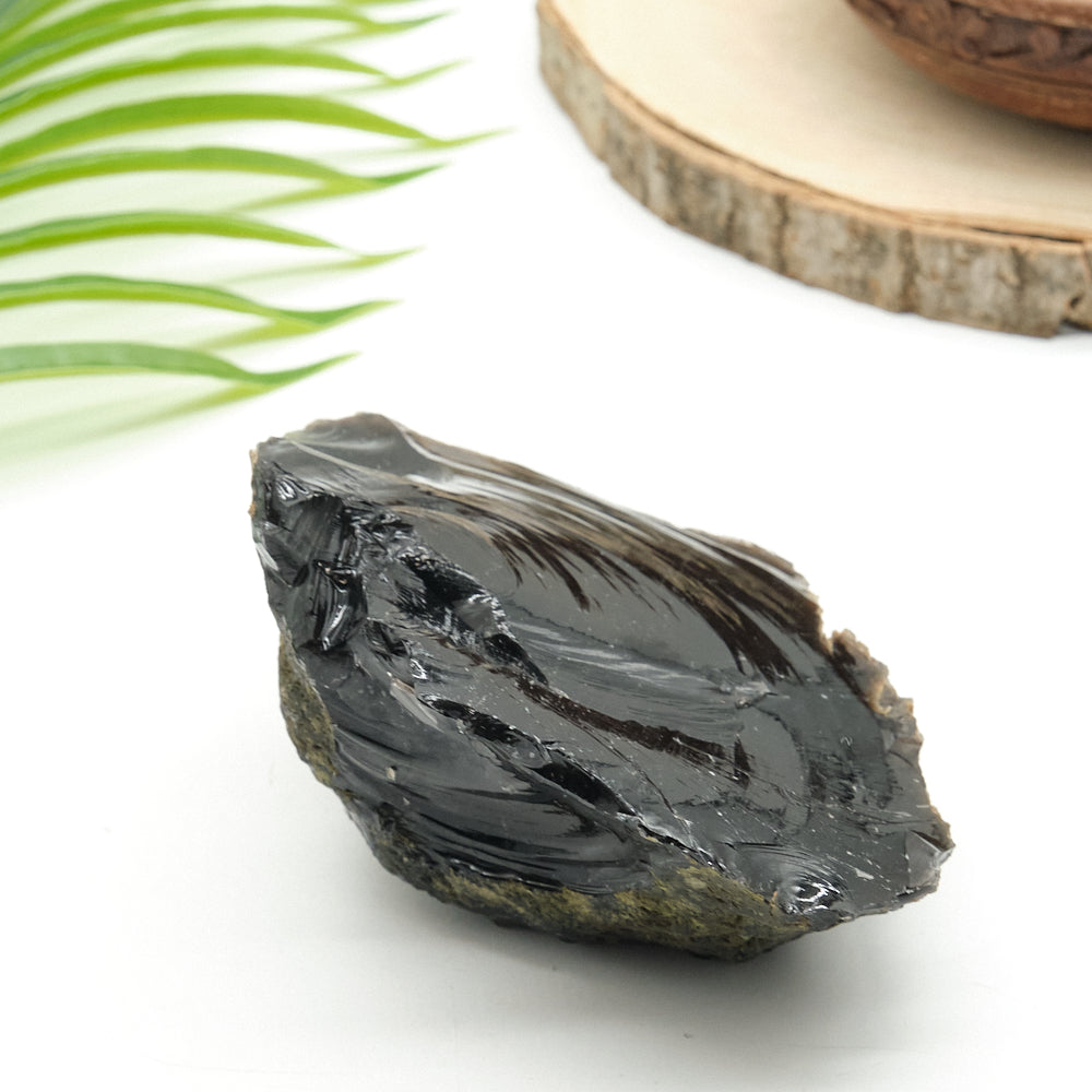 Black obsidian stone on a white surface with green leaves and a wooden slice in the background