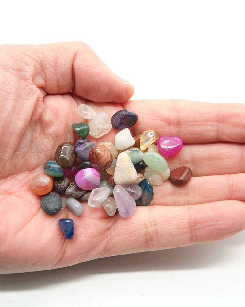 Hand holding a small collection of multicolored stones on a white background