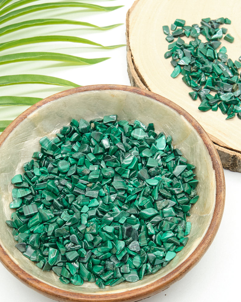 Green Malachite stone chips in a ceramic bowl with green leaves in the background