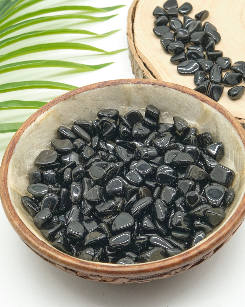 Black Obsidian stones in a ceramic bowl with green leaves in the background
